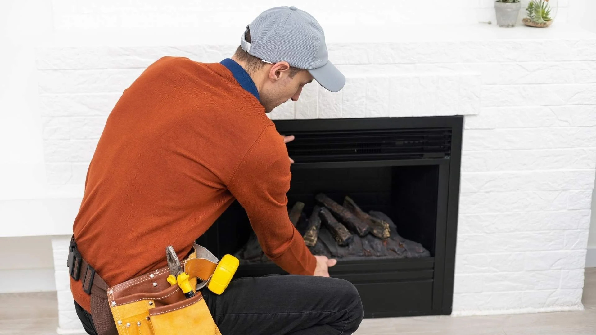 man performing inspection and maintenance onto a gas insert fireplace in a orange long sleeve t-shirt wearing a tool belt
