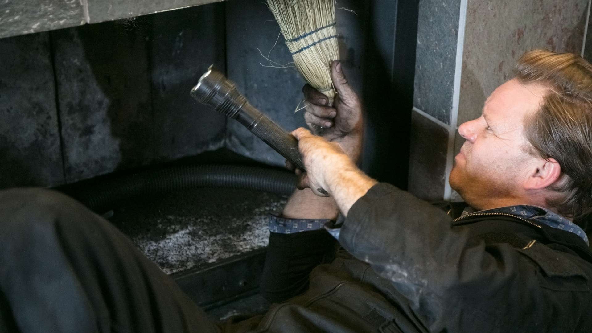 man in black uniform cleaning the innerworks of a fireplace
