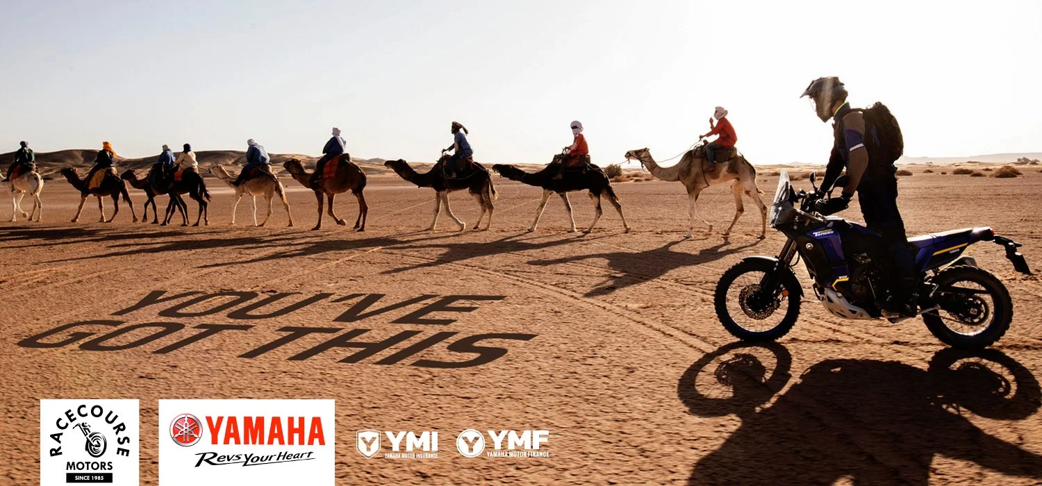 A group of people riding camels in a desert with the words 'YOU'VE GOT THIS' written on the sand. A motorcyclist in gear riding a Yamaha motorcycle in the foreground, with logos of RACECOURSE Motors, Yamaha, YMI, and YMF.