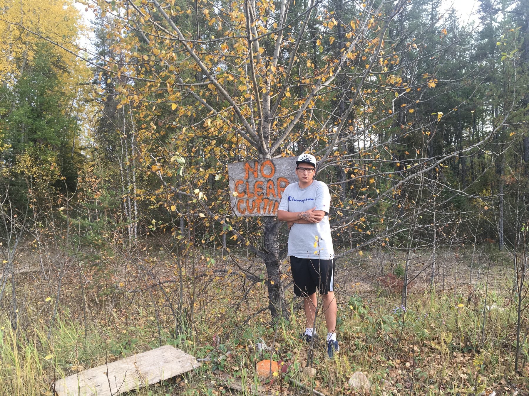 Dakota Bear standing beside a No Clear Cutting sign in the forest on Treaty 6 territory