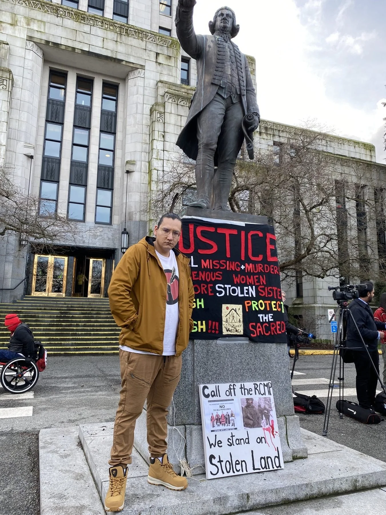 Dakota Bear at Vancouver City Hall beside a Justice for Missing and Murdered Indigenous Women banner and a We Stand on Stolen Land sign