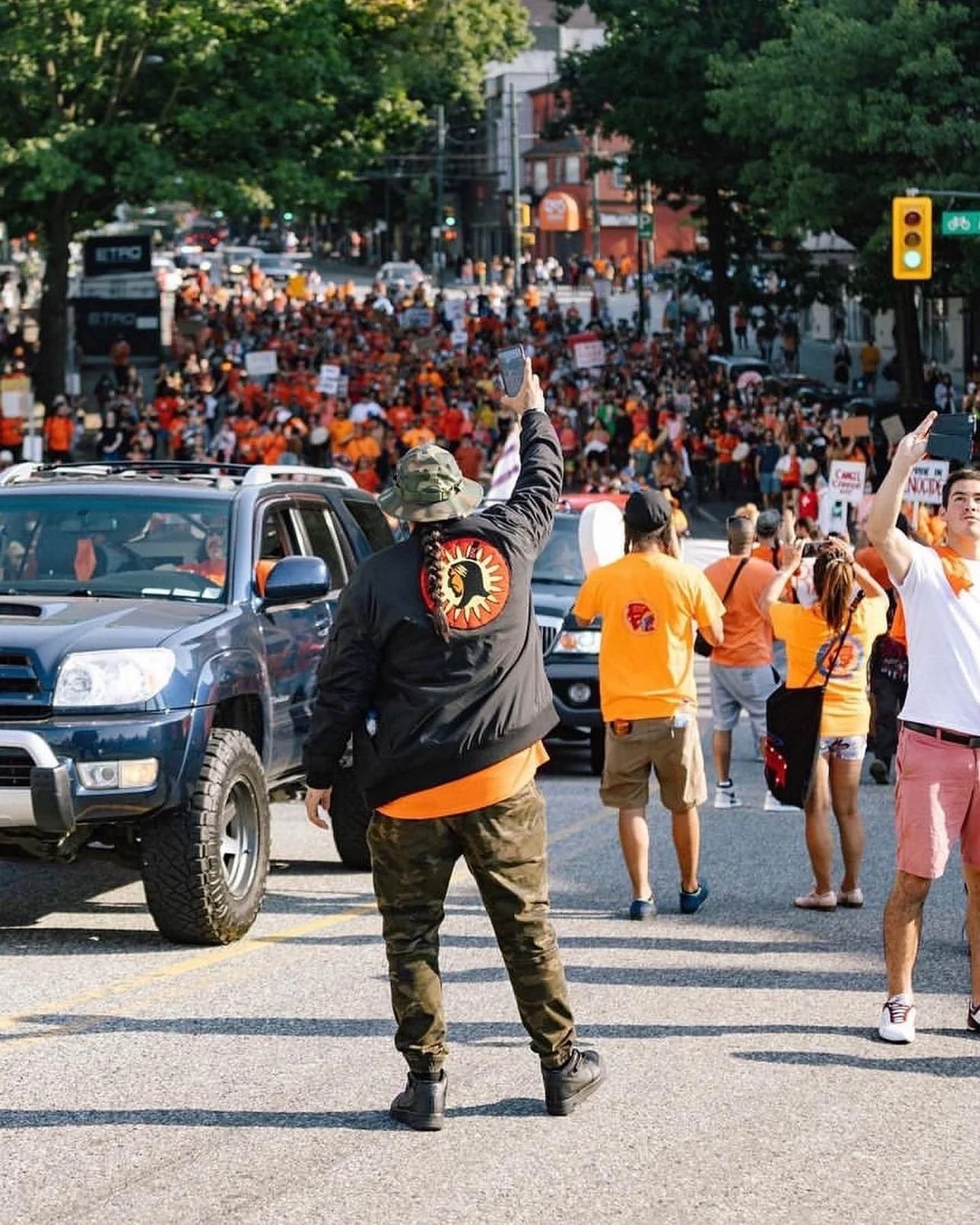 Dakota Bear in a Big Bear jacket raising his hand as thousands in orange march for Cancel Canada Day in Vancouver