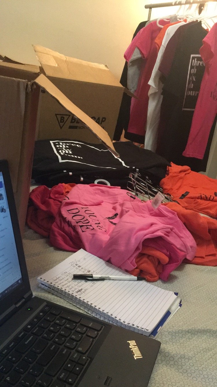 The first 30604 Apparel shirts laid out at home next to a laptop and order notebook, 2015