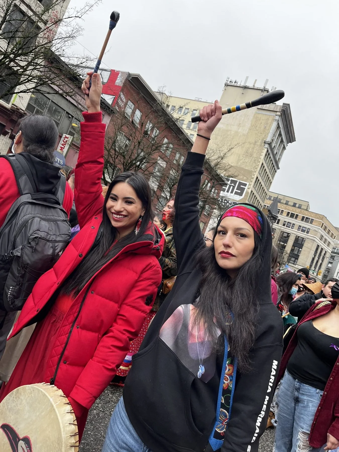 Two Indigenous women raising drumsticks at a march in downtown Vancouver