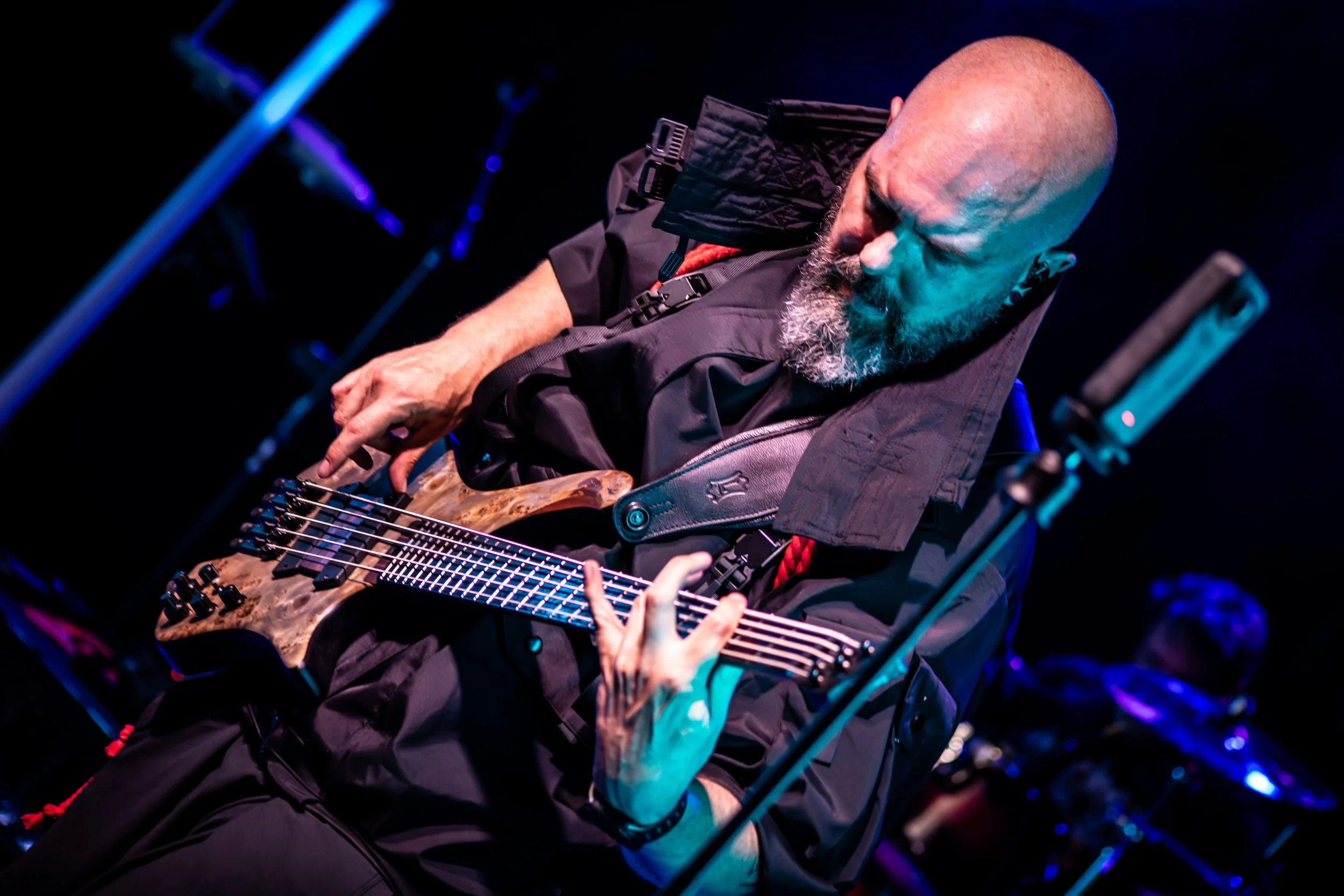 A bald man with a beard playing an electric guitar on stage under colorful lights.
