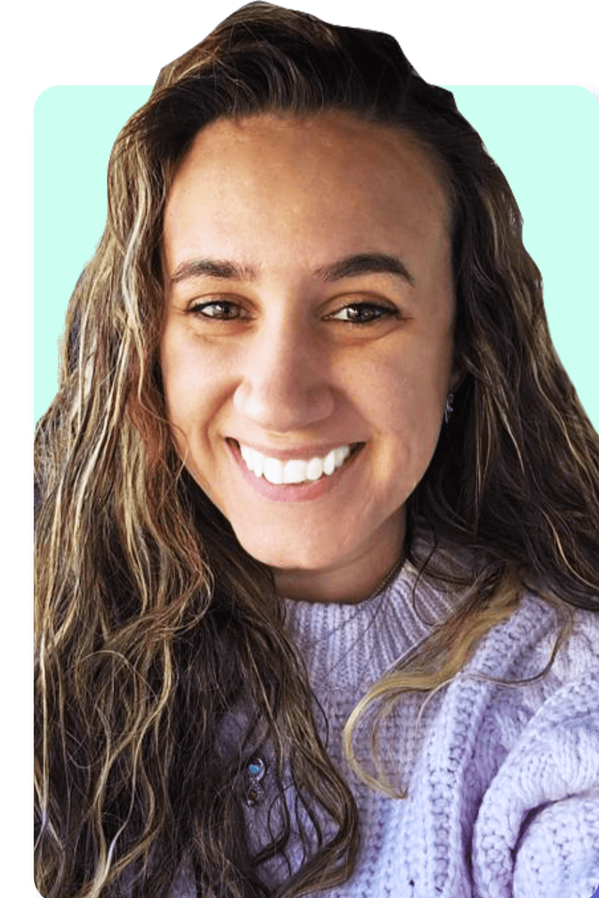 Close-up of a smiling woman with long, wavy brown hair wearing a lavender sweater.