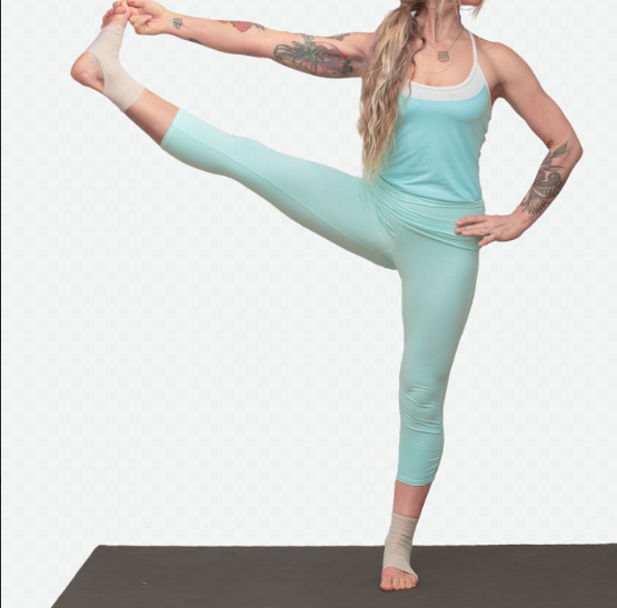 Person in teal yoga outfit performing standing leg stretch pose on mat.