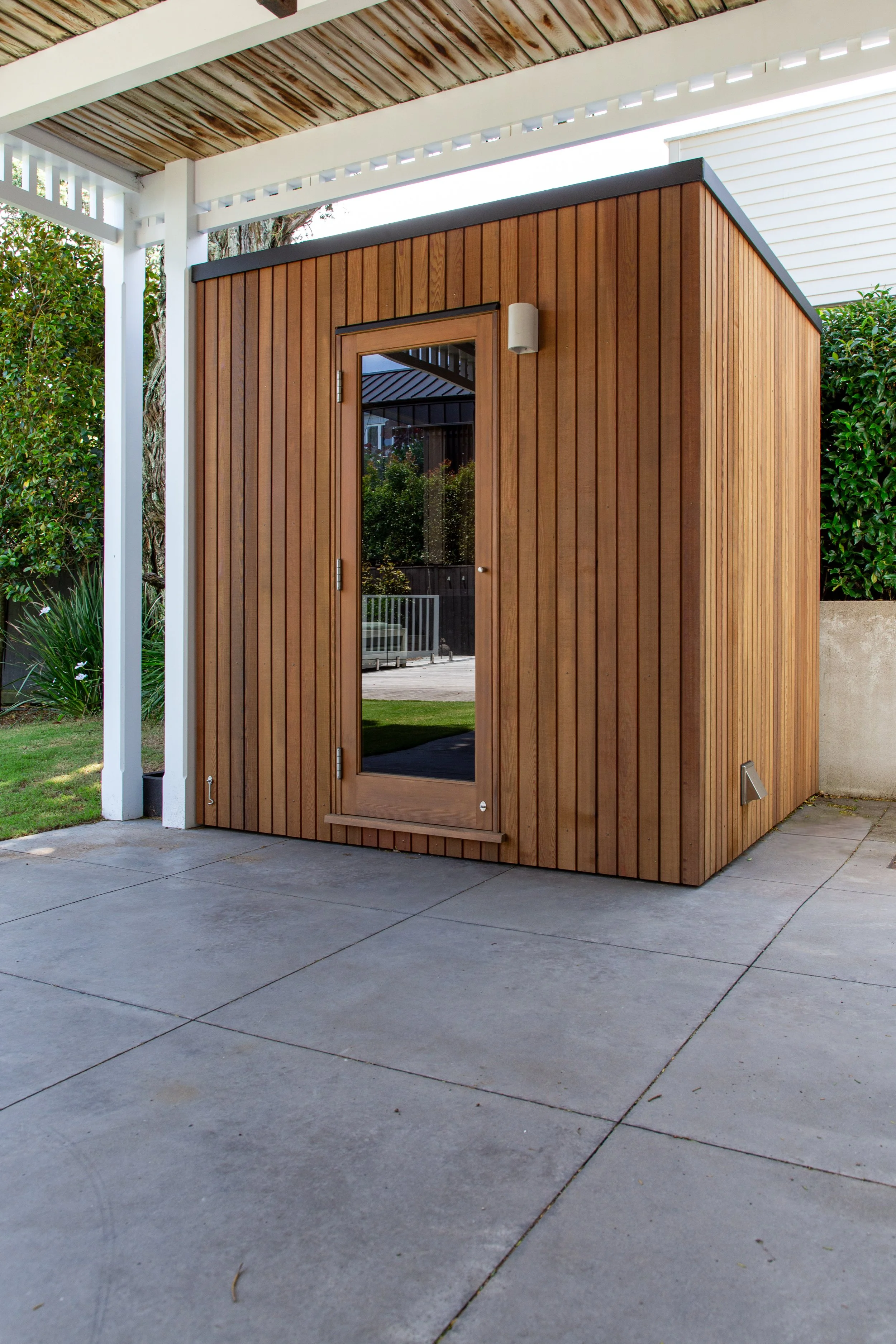 Outdoor cedar sauna situated in a mount eded garden court yard, designed for easy access and convenience for an everyday sauna bather