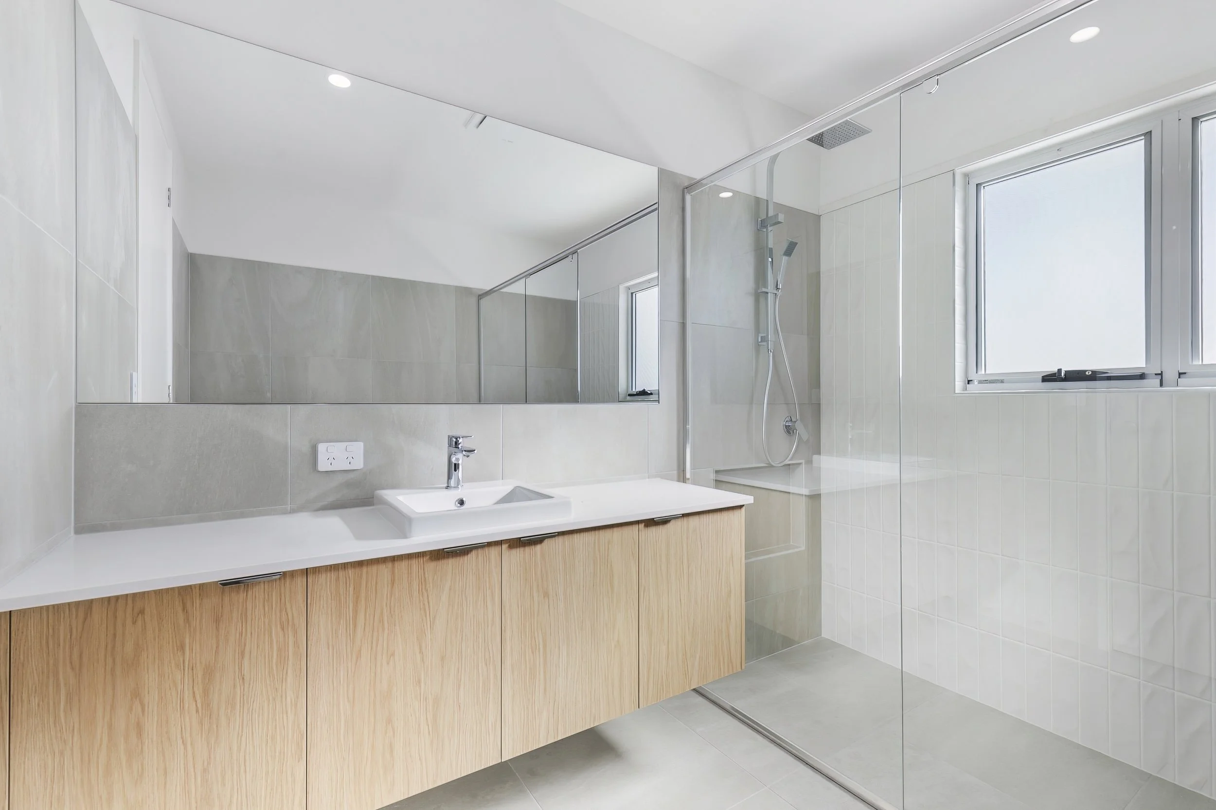 Modern bathroom with a vanity, sink, large mirror, and walk-in shower with glass enclosure and window.
