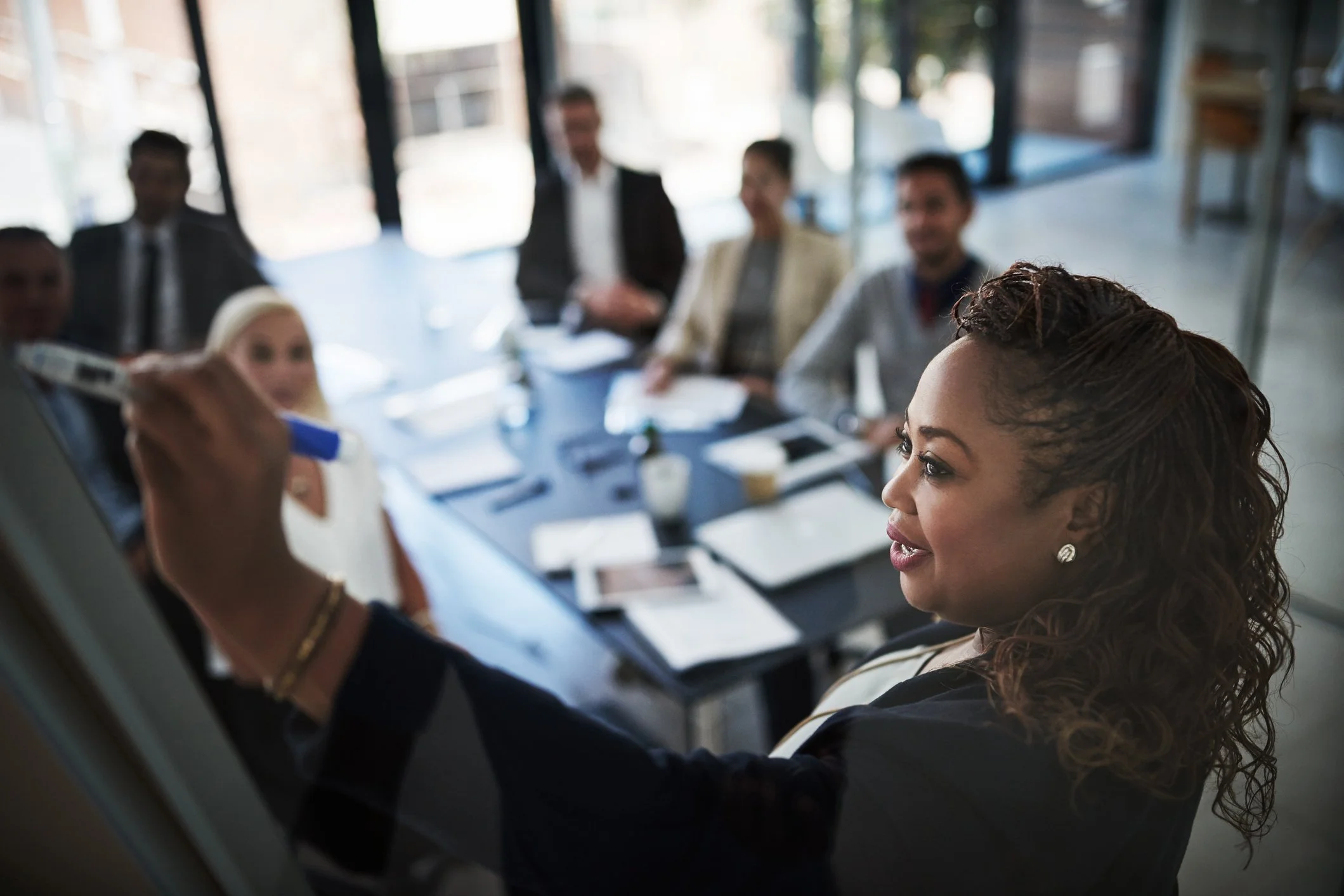 A diverse group of professionals sitting around a conference table in a modern office, engaging in a meeting or discussion.