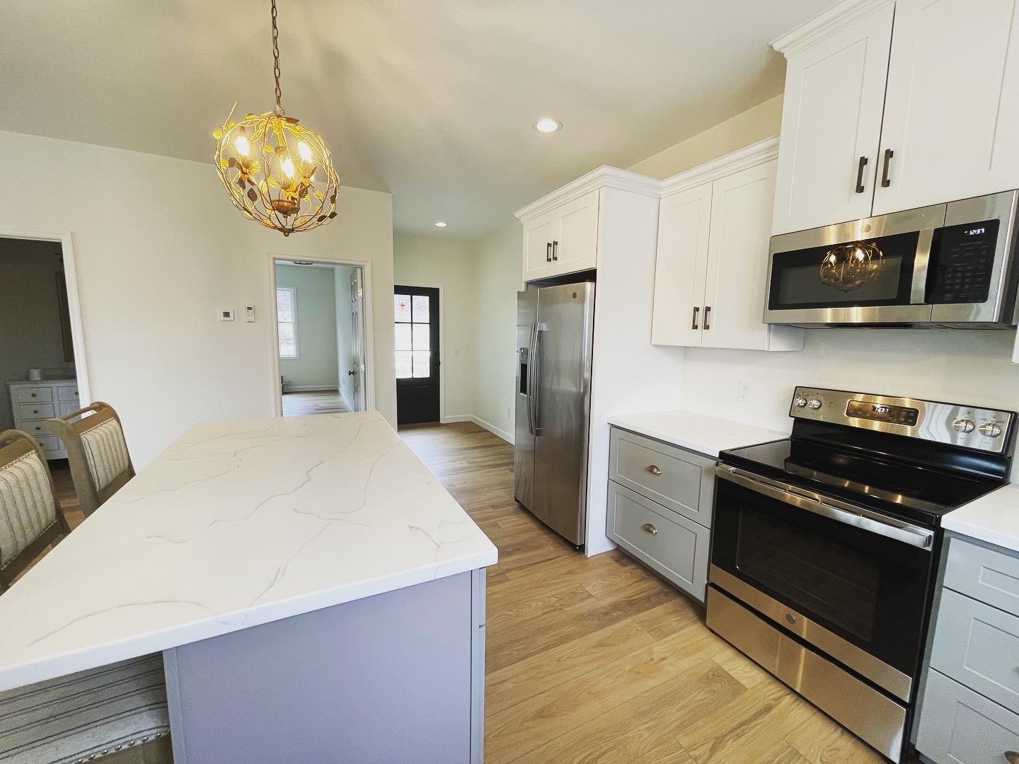 Modern kitchen with white shaker cabinets, stainless steel appliances, light wood flooring, and a large island with quartz countertops and upholstered bar stools.