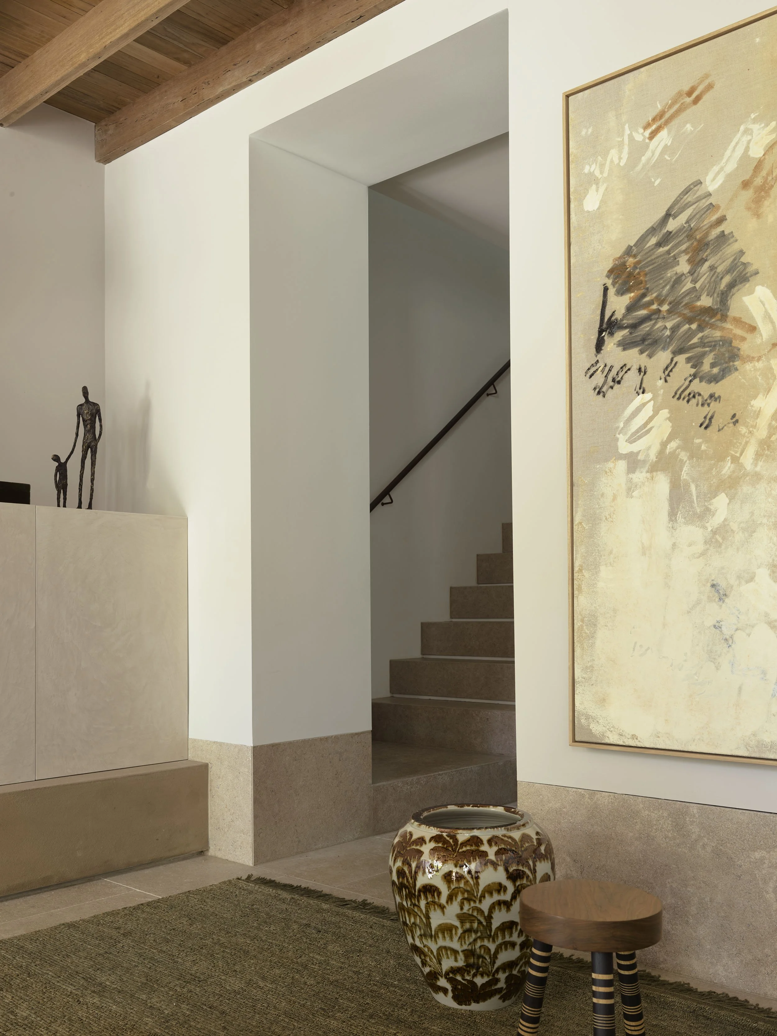 Interior view of a modern house with stairs, abstract artwork on the wall, a decorative vase, and small sculptures on a cabinet.