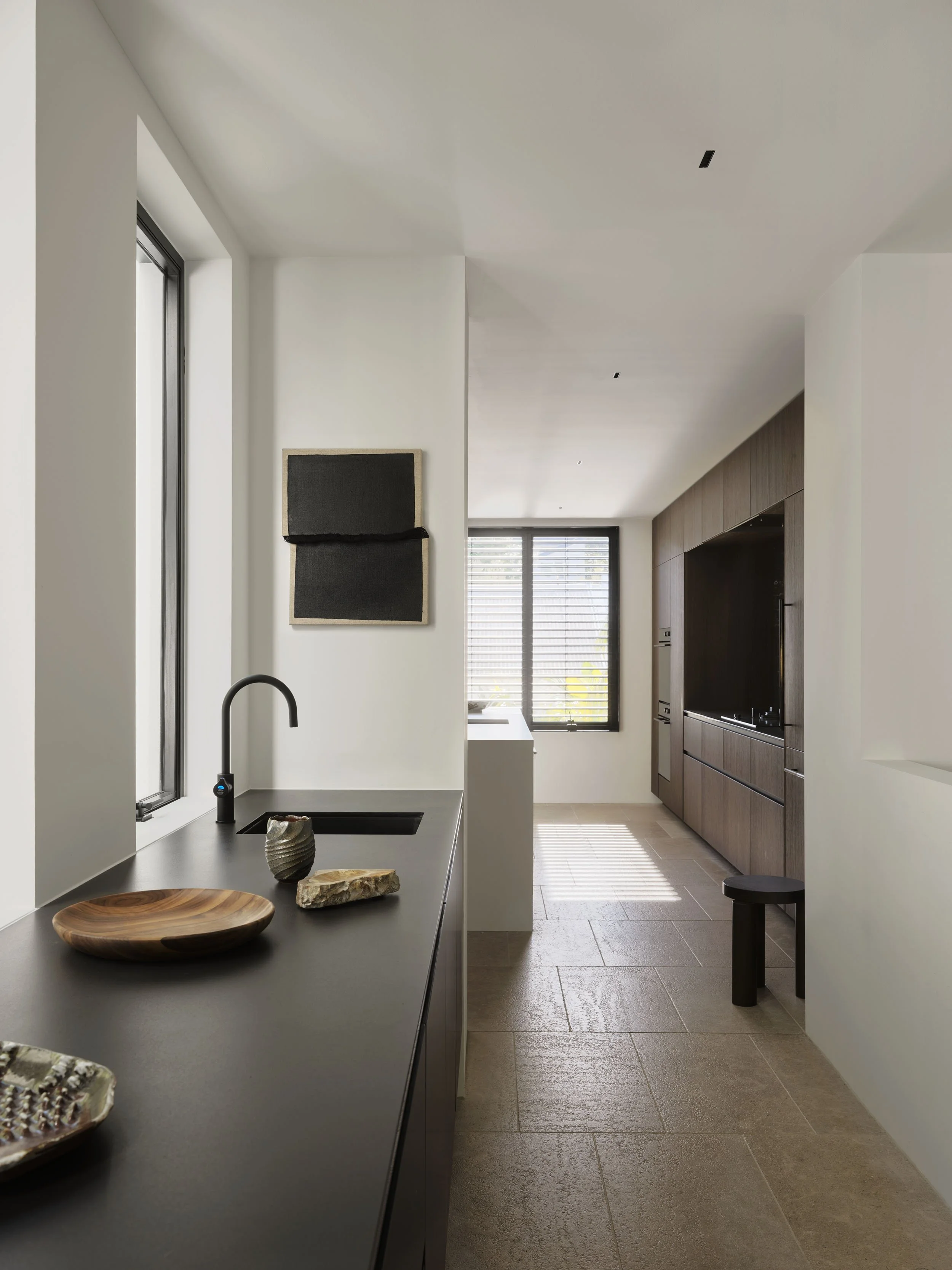 Modern kitchen with a black countertop, ceramic bowls, a black faucet, a window, and wooden cabinetry.
