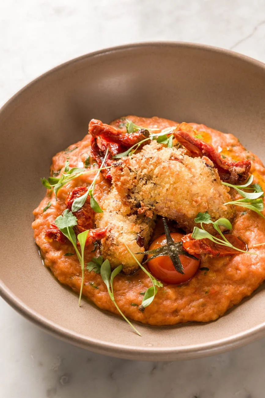 Prato de comida com molho de tomate, um filé empanado, tomate cherry e folhas verdes.