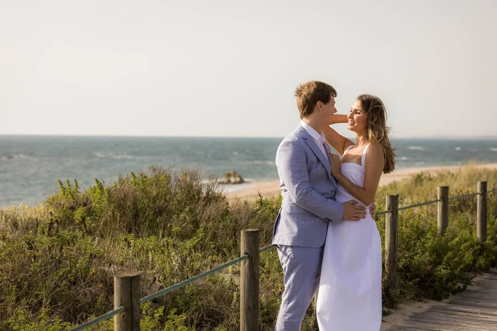 Casal em roupas de casamento, sorrindo e se abraçando na praia.