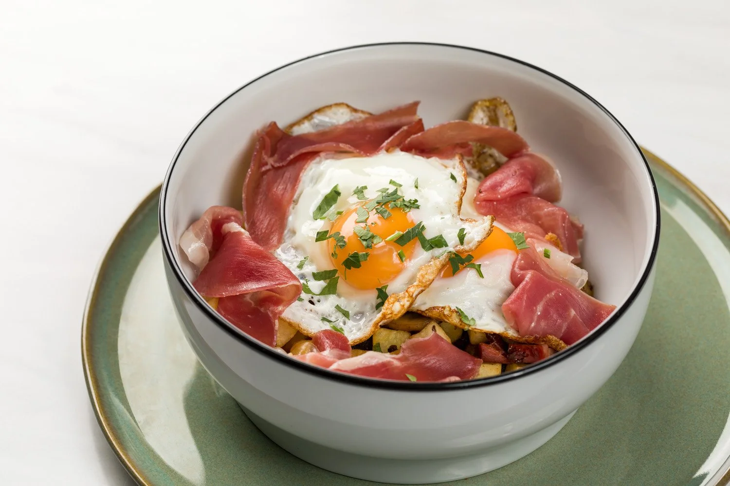 Prato com ovo frito, presunto e queijo em uma tigela branca sobre um prato verde.