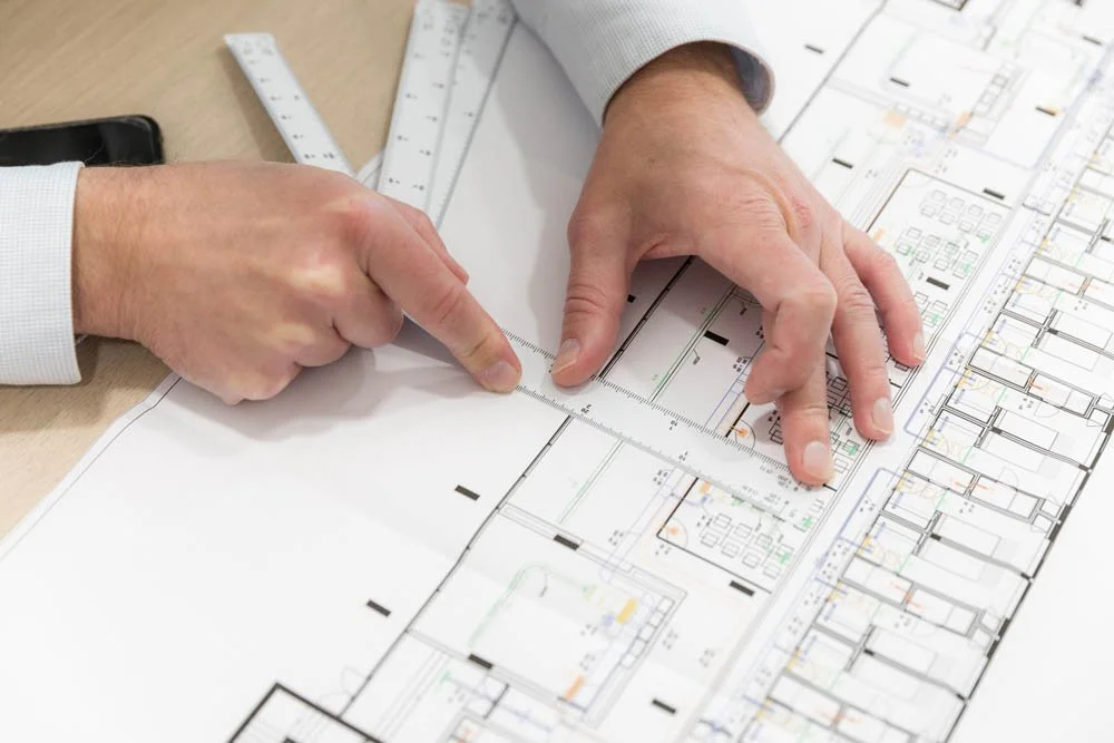 Pessoa usando régua para medir planta arquitetônica em uma mesa de trabalho.