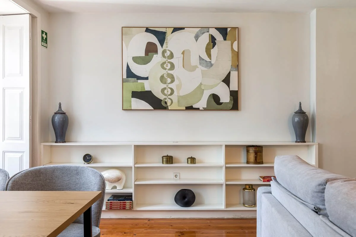 Sala de estar com estante branca decorada com vasos, livros e objetos decorativos, com quadro de arte moderna na parede acima.