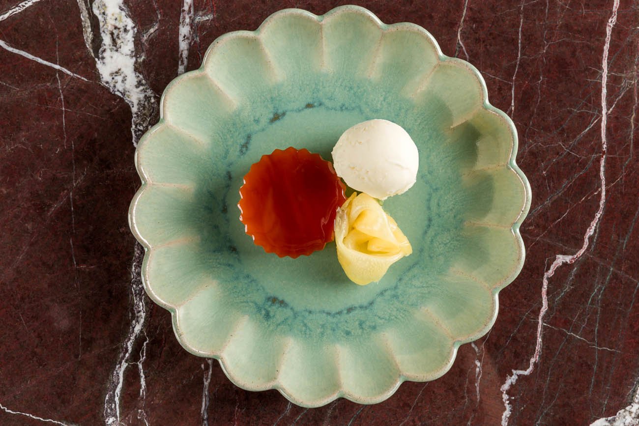 Sorvete de baunilha com mel, geleia de amora e uma fatia de limão no recipiente, tudo em um prato verde