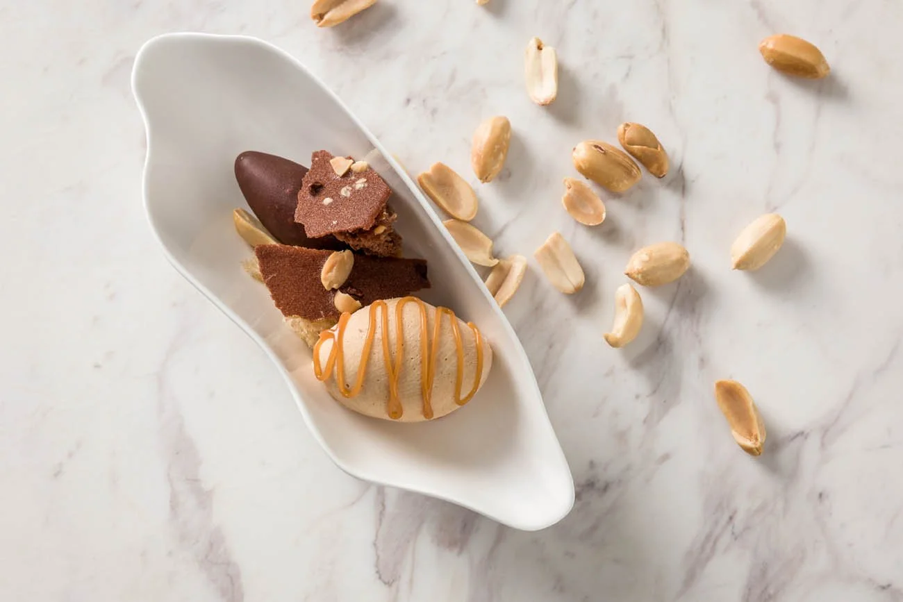 Sobremesa com sorvete, biscoitos de chocolate e castanhas em uma travessa branca sobre uma mesa de mármore