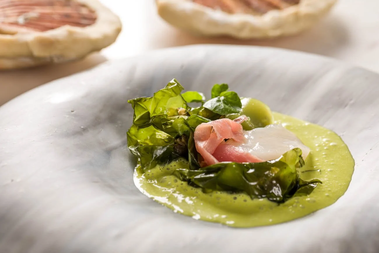 Prato de comida com folhas verdes, fatias de presunto, e molho verde, em prato branco