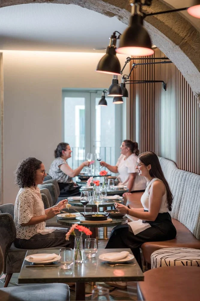 Grupo de mulheres conversando e fazendo um brinde enquanto jantam em restaurante sofisticado.