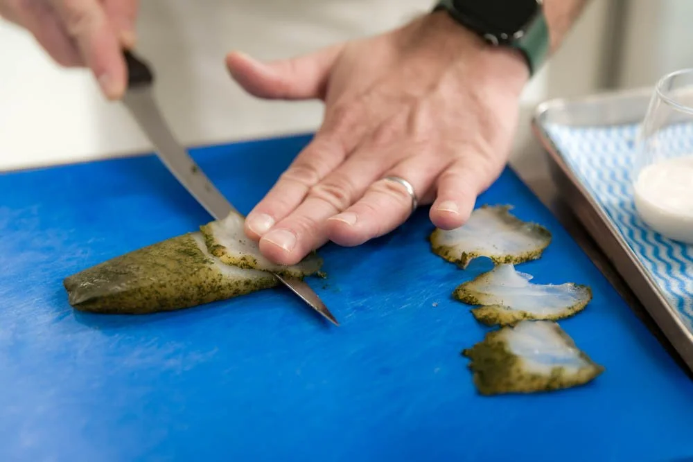 Pessoa cortando lula limpa em uma superfície azul, com uma tigela com algum ingrediente ao lado.