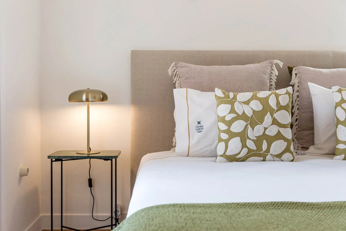 Cama com travesseiros decorativos e almofadas em quartos com decoração em tons neutros e uma luminária dourada