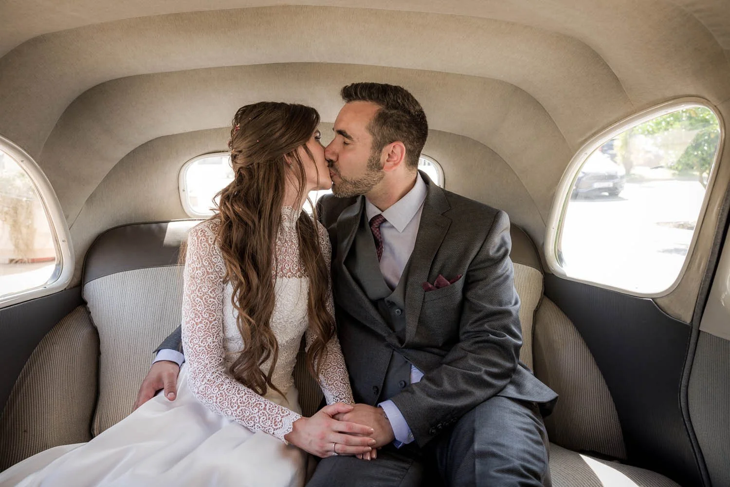 Casal de casamento beijando no interior de um carro antigo, com vestido de noiva e terno
