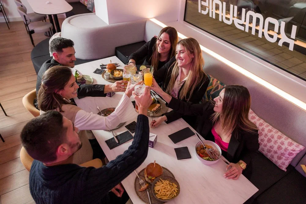 Grupo de amigos sorridentes comemorando com drinks e comida em um restaurante.