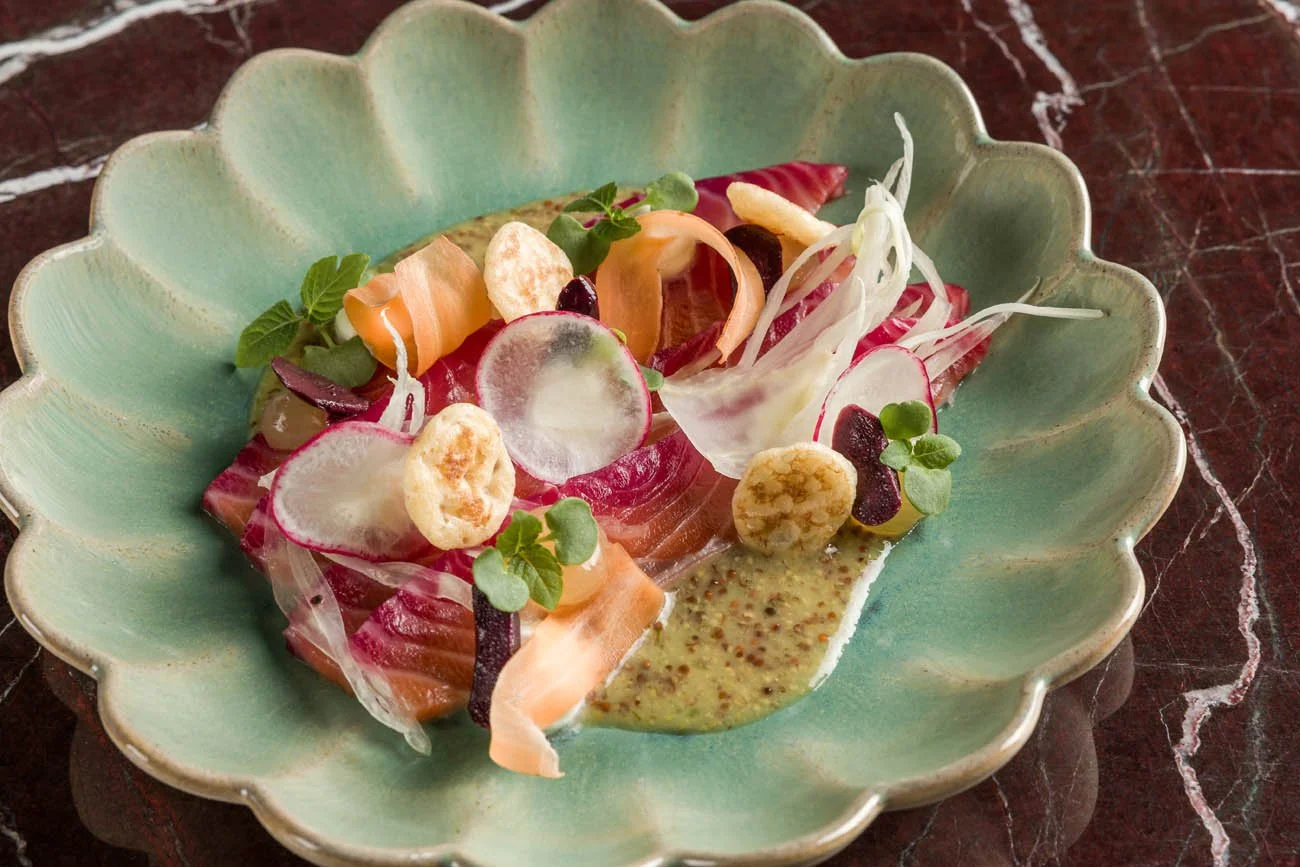 Salada colorida com fatias de radicchio, fatias de cenoura, folhas verdes, brotos, pimentões, vinagrete em prato verde decorativo com fundo de mármore escuro.