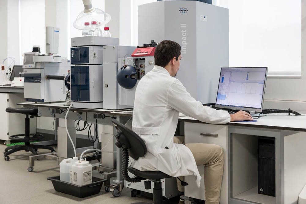 Pesquisador trabalhando com equipamento de laboratório e computador em ambiente de pesquisa científica.