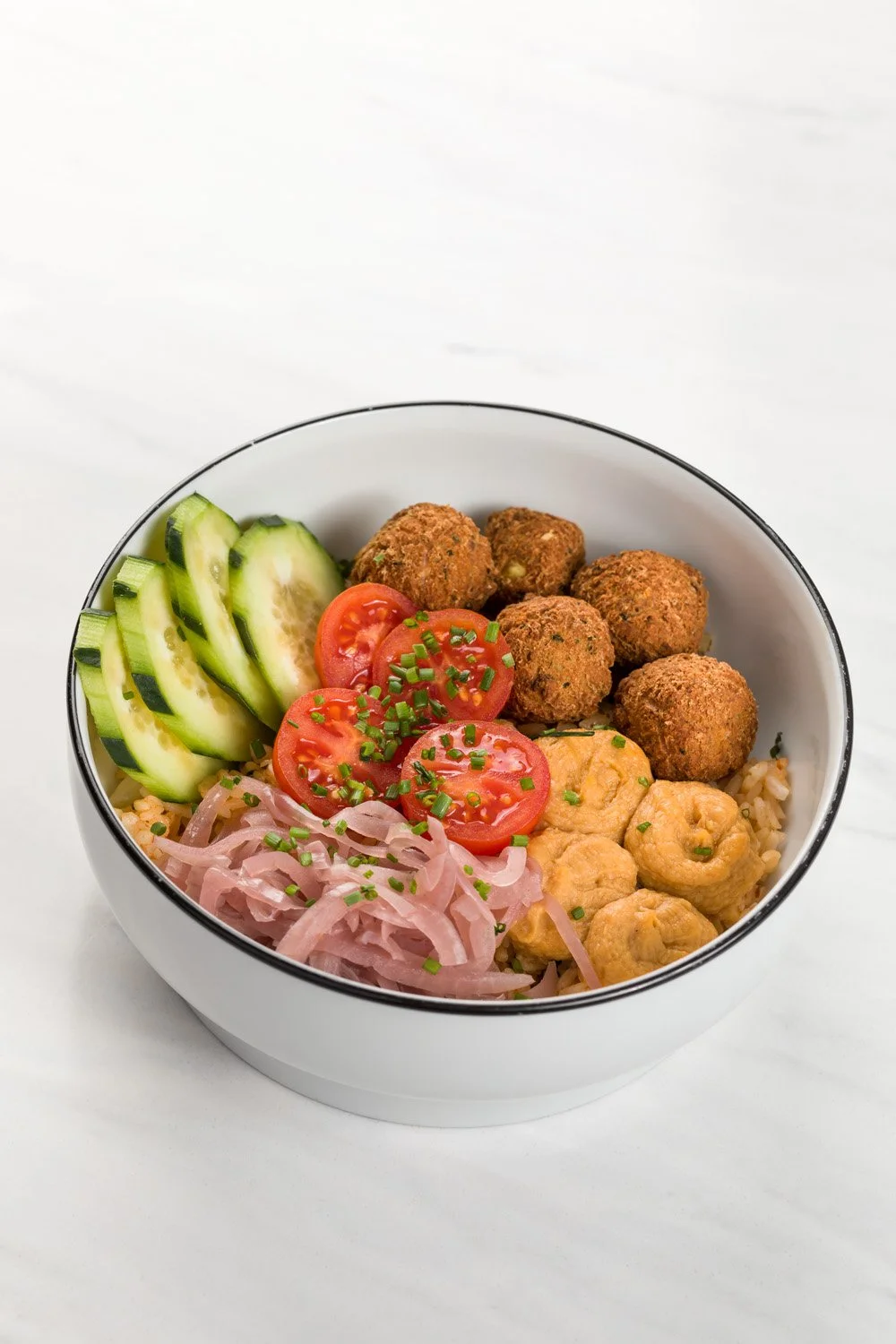 Salada com tomate, pepino, cebola, almôndegas e pedaços de frango em uma tigela branca com uma borda preta.