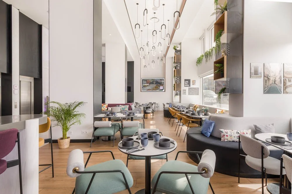 Interior de restaurante ou café com mesas e cadeiras modernas, decoração com plantas, iluminação pendente e paredes decoradas.