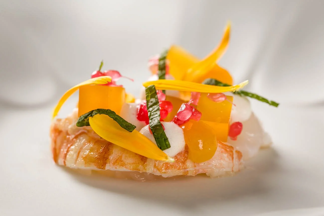 Prato de peixe com molho, decorado com pimentões amarelos, folhas verdes, sementes de romã e espuma branca.