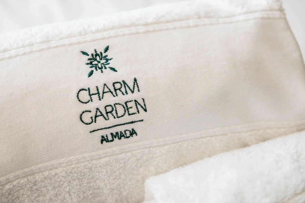 Etiqueta de tecido com o logo e nome Charm Garden Almada, em detalhes.