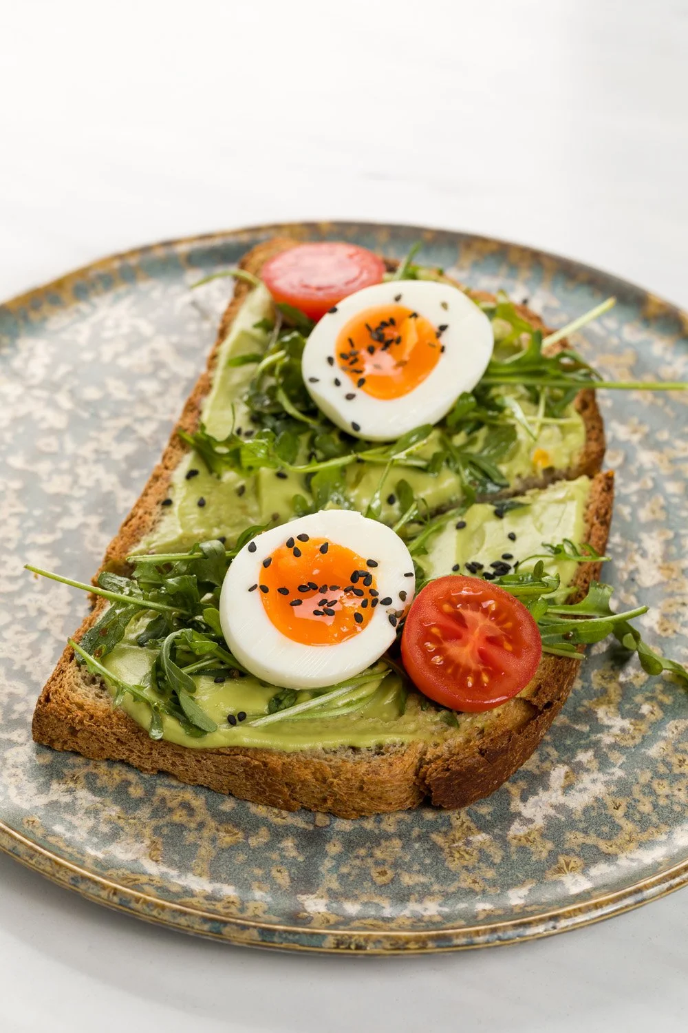 Torrada com abacate, ovos cozidos, tomate cereja, brotos e sementes pretas