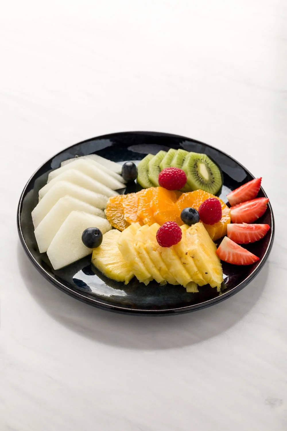 Prato com variedade de frutas fatiadas, incluindo melão, uva, kiwi, abacaxi, morango e manga.