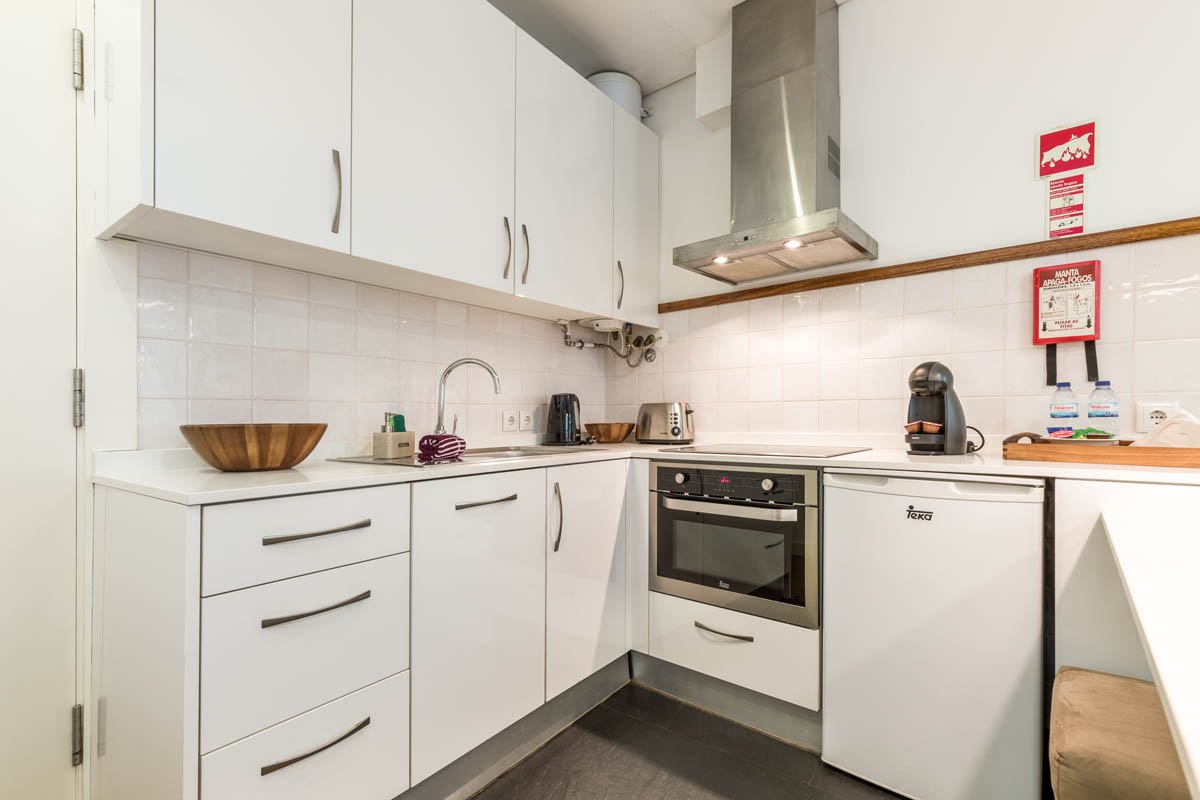 Cozinha com armários brancos, cooktop, forno integrado, micro-ondas, ventilar, pia com torneira, e utensílios na bancada.