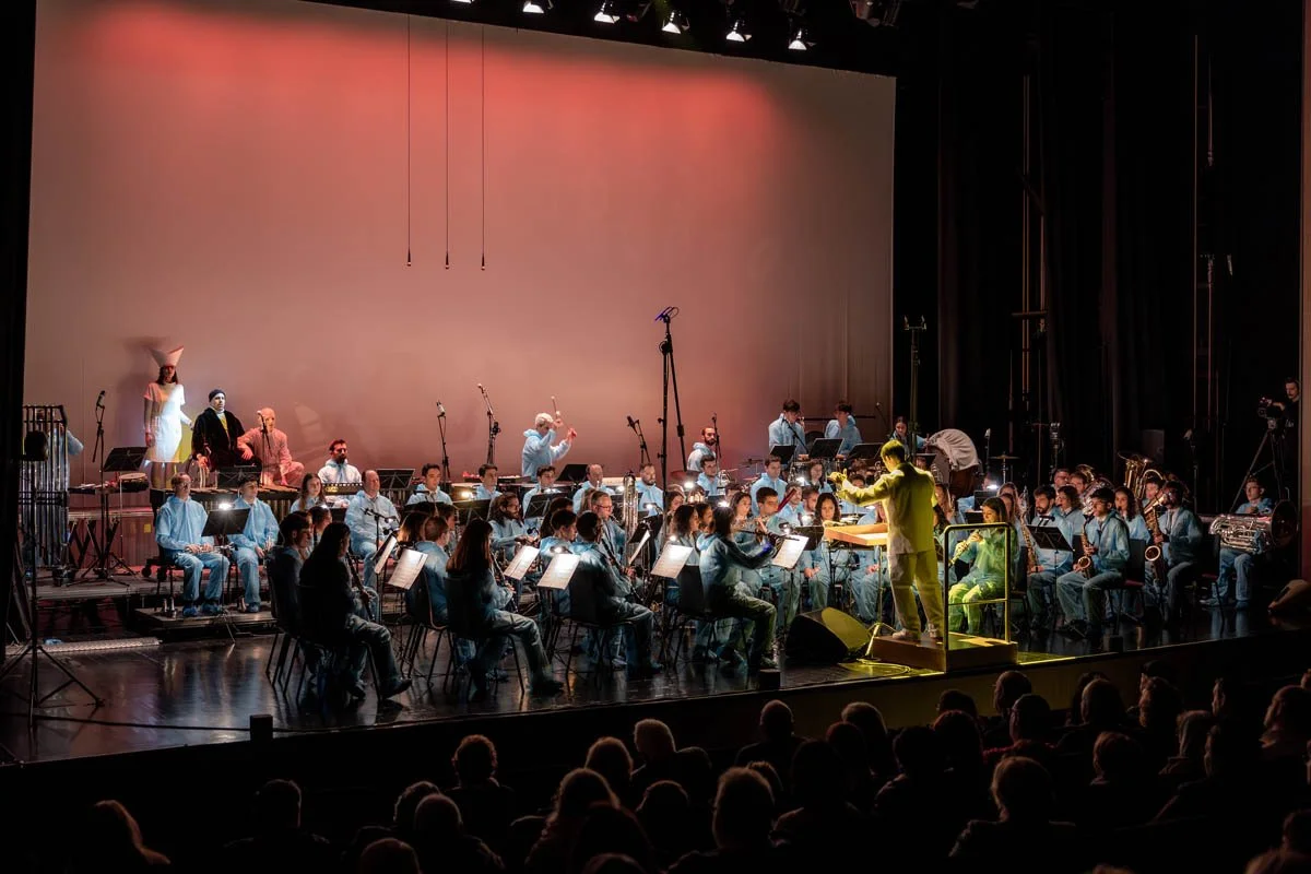 Orquestra tocando no palco de um teatro com público assistindo.