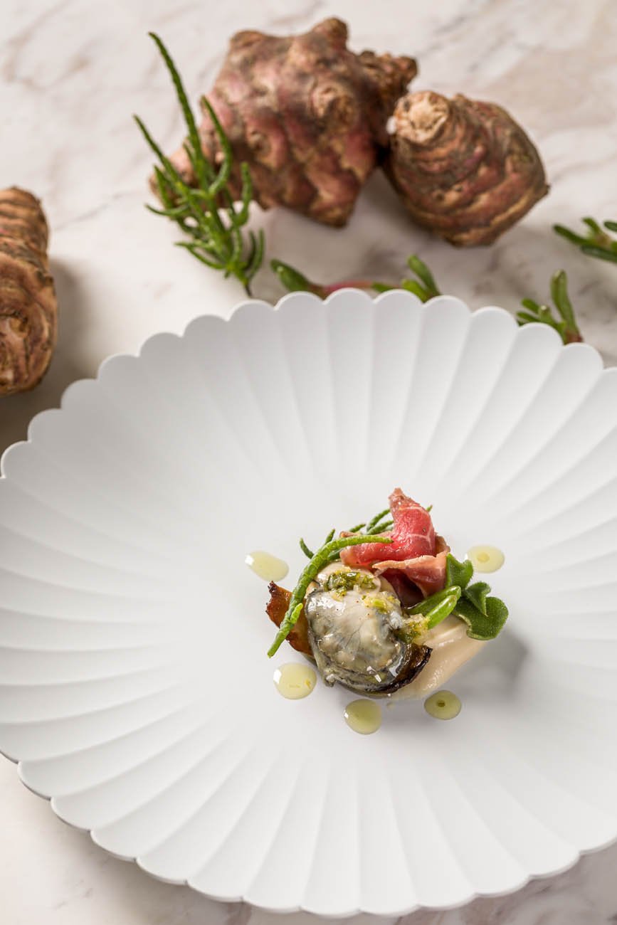 Prato sofisticado com frutos do mar, rodelas de ervas verdes e gotas de molho, servido em prato branco decorativo.