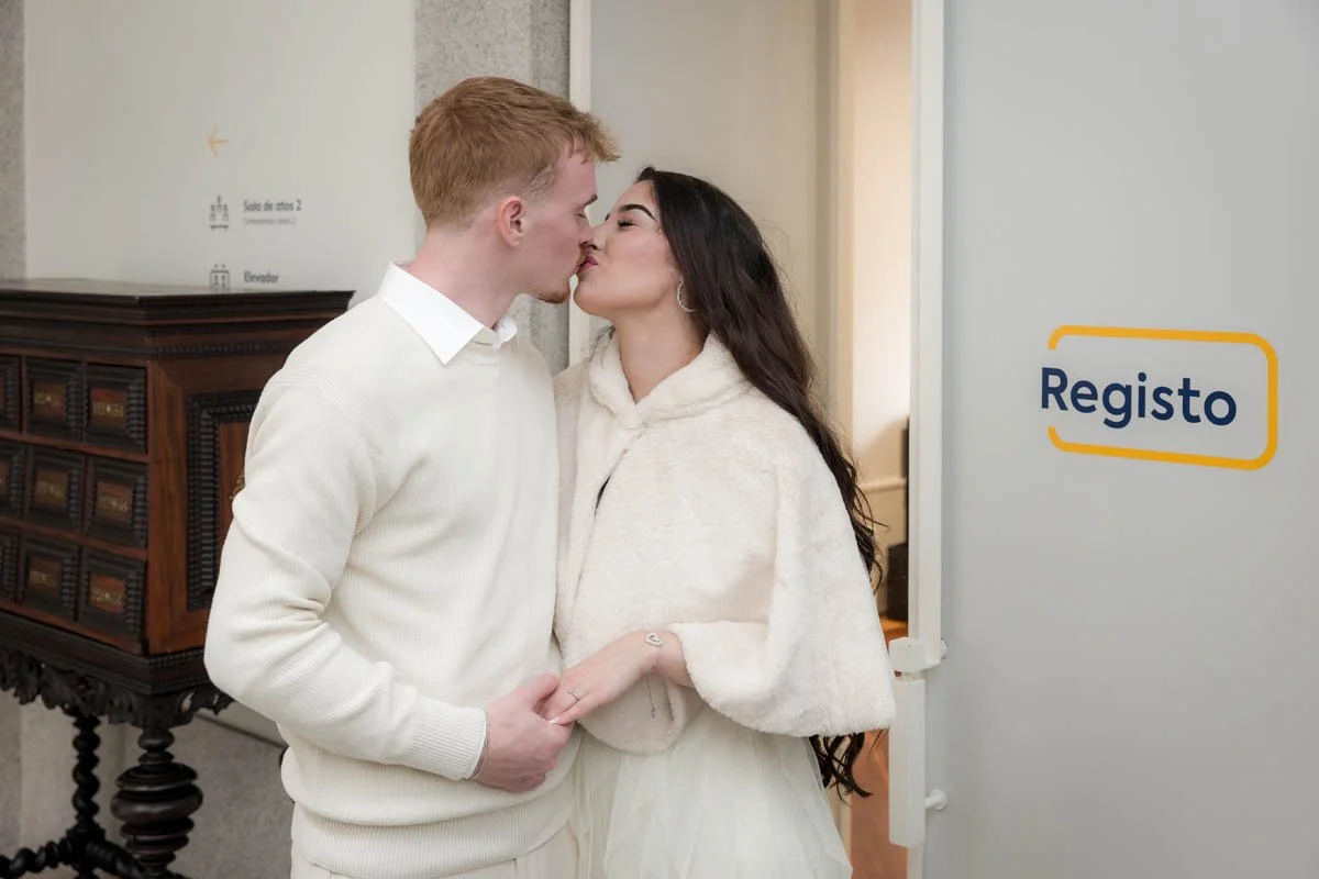 Casal se beijando na entrada de um espaço com o sinal 'Registo' ao lado.