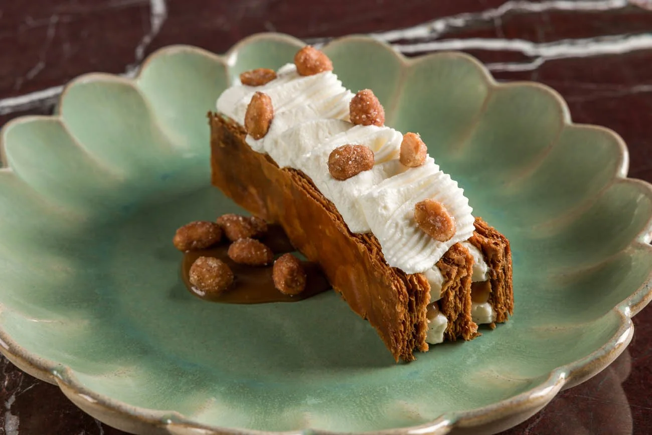 Torta de churros com cobertura de chantilly e cereais, servida em um prato decorativo verde.