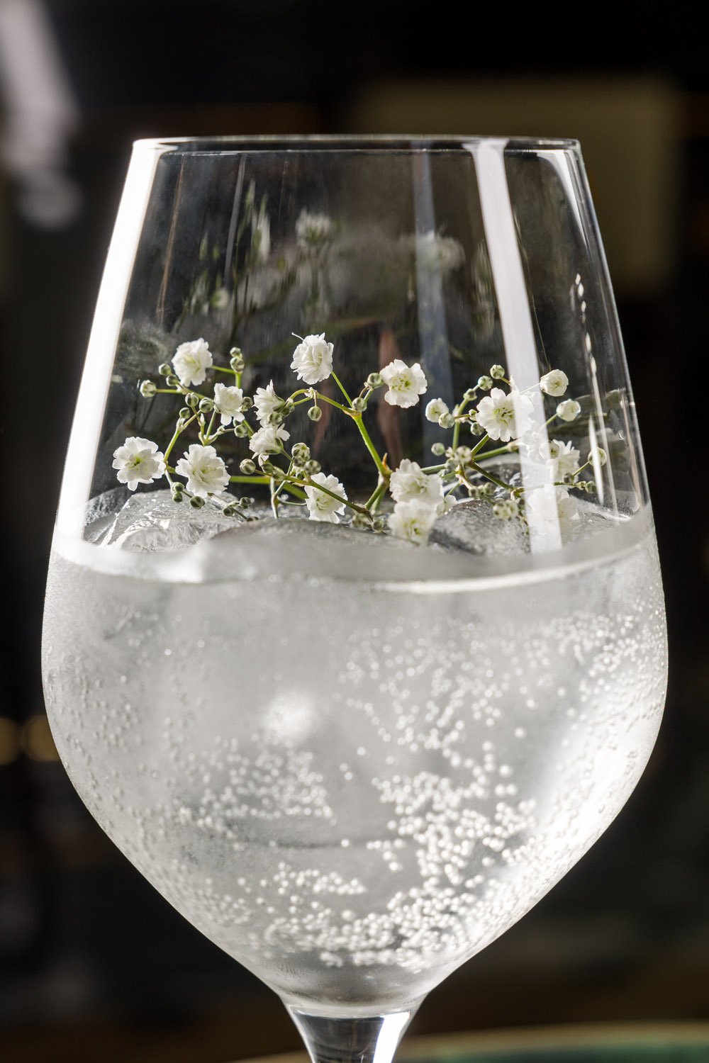 Vaso de coquetel transparente com gelo e uma flor branca decorativa dentro.
