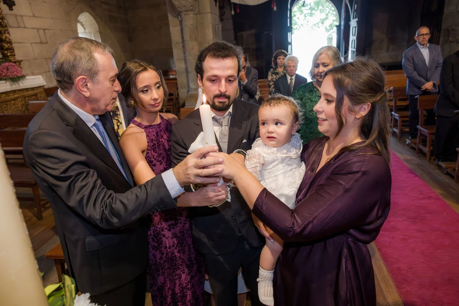 Família reunida em cerimônia religiosa acendendo vela com alegria e reverência.