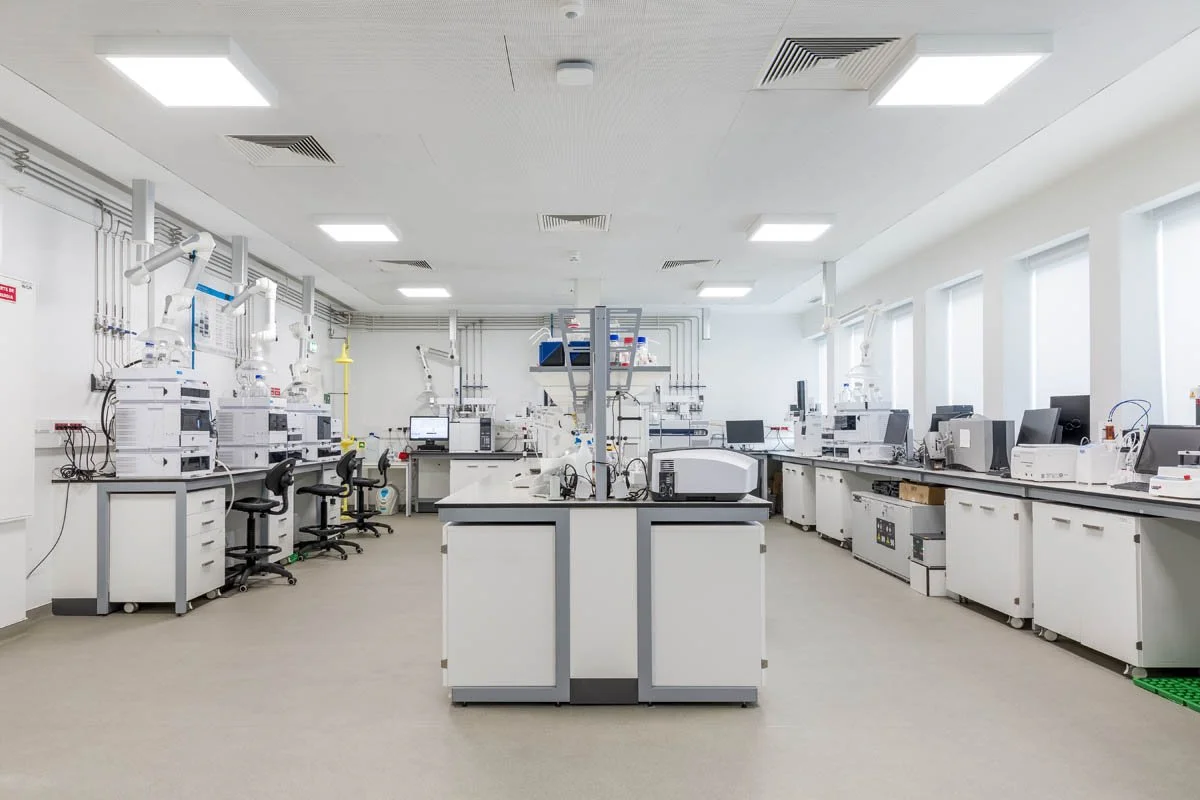 Laboratório limpo com bancadas e equipamentos de pesquisa científica, várias máquinas e computadores.