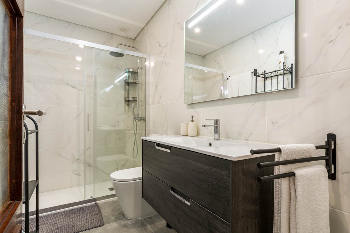 Banheiro moderno com pia, espelho grande, toalha pendurada, box de vidro com ducha e luminária no teto.