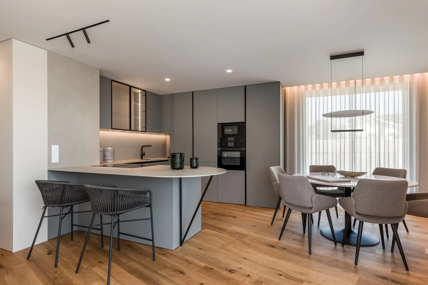 Cozinha moderna com mesa de jantar e cadeiras na área de estar, iluminação suave e cortinas transparentes.
