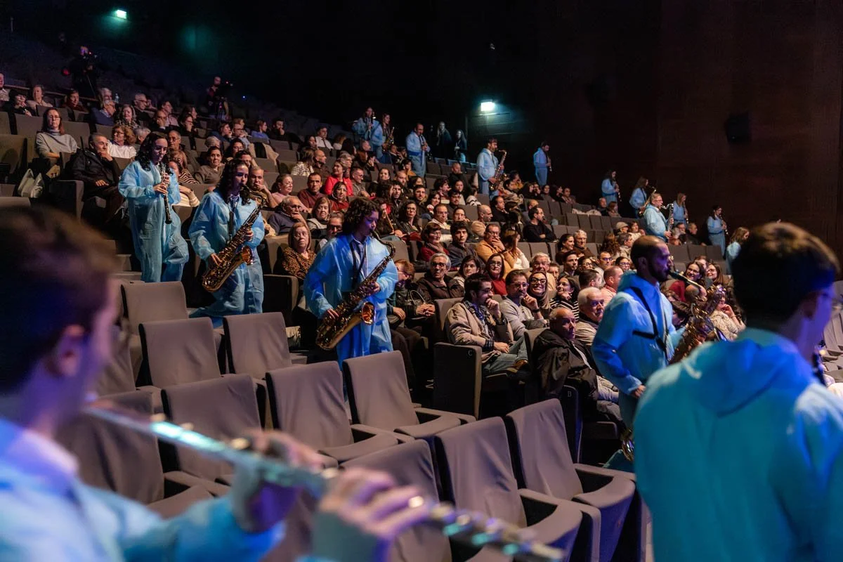 Orquestra tocando instrumentos em um teatro com público assistindo.