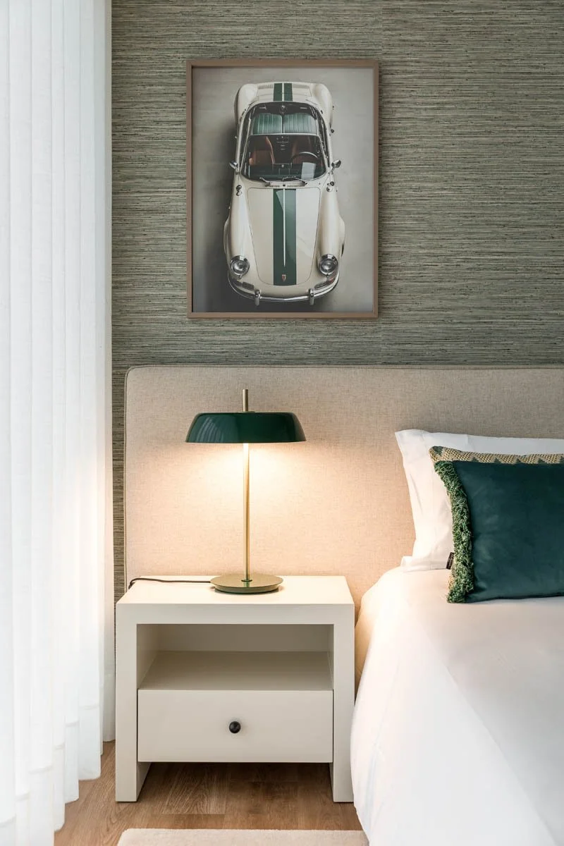 quarto com cabeceira de cama, luminária de mesa e quadros com carro clássico na parede